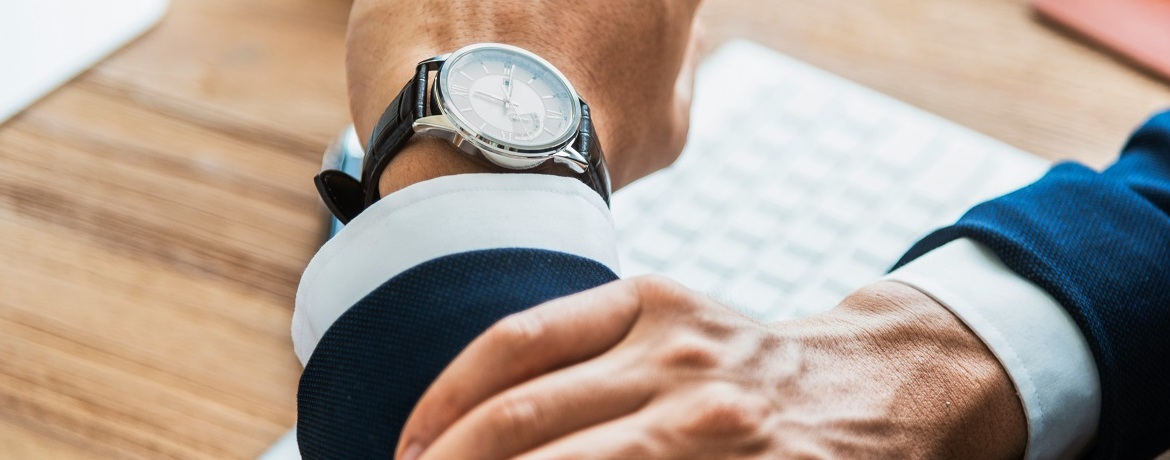 Geschäftsmann prüft die Uhrzeit am Arbeitsplatz – Symbol für Steuerfristen und Zeitmanagement.