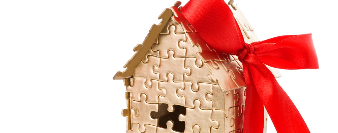 Modellhaus aus Puzzleteilchen mit Geschenkschleife- Symbolisch für das Thema Immobilienübergabe_Schenkungsteuer